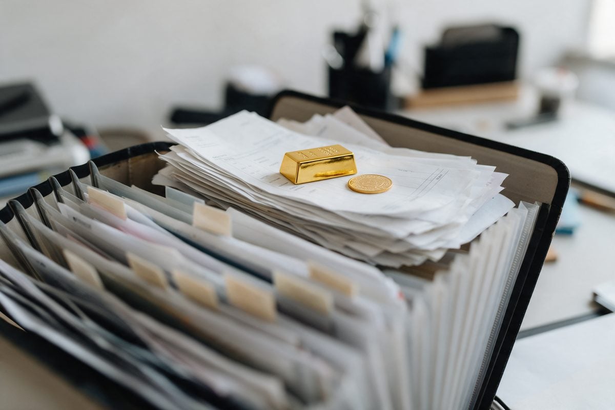 Carpeta con facturas y certificados junto a un lingote de oro: documentacion ordenada